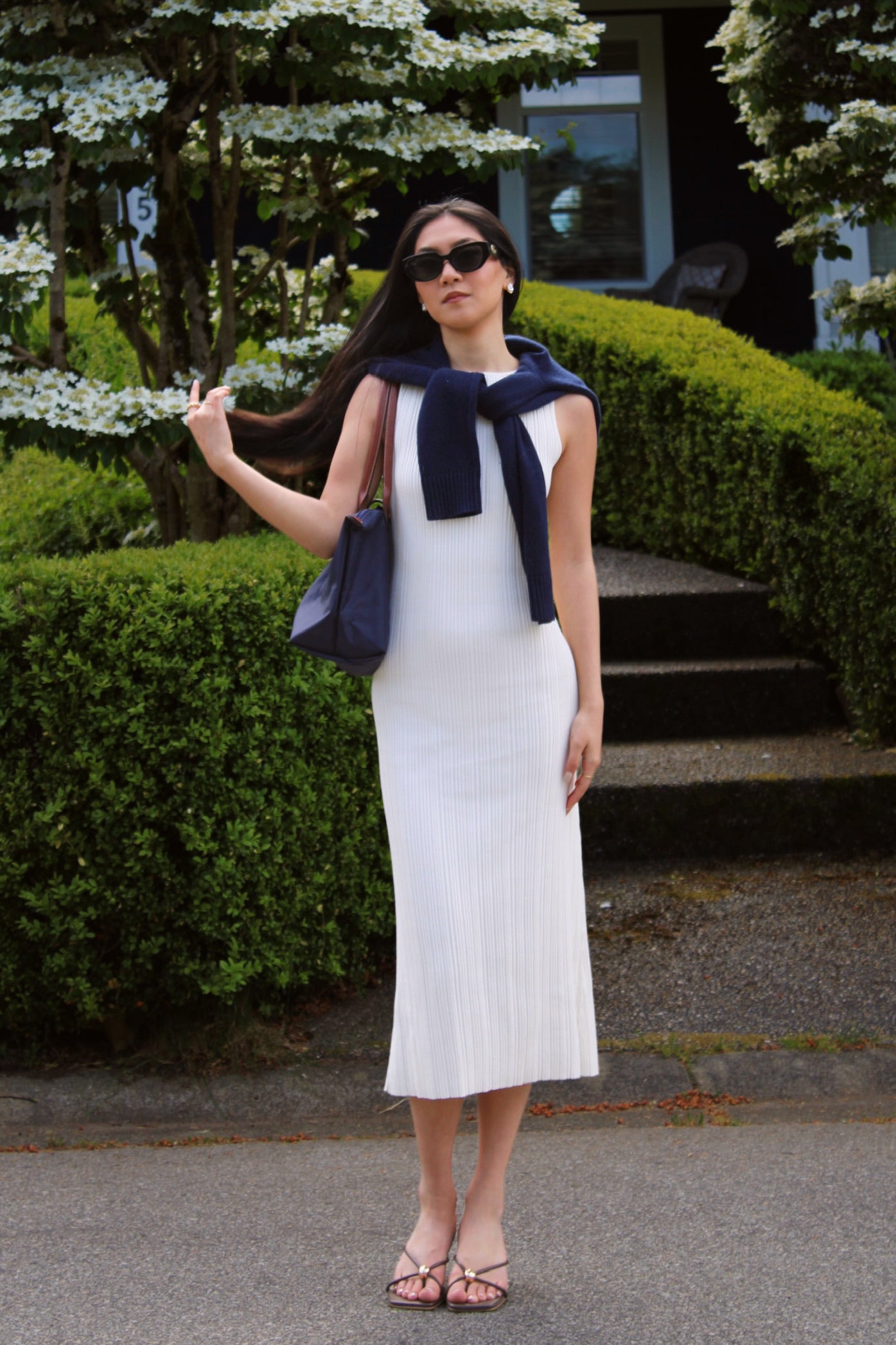 Woman in a white lounge dress with a navy cardigan standing outdoors.