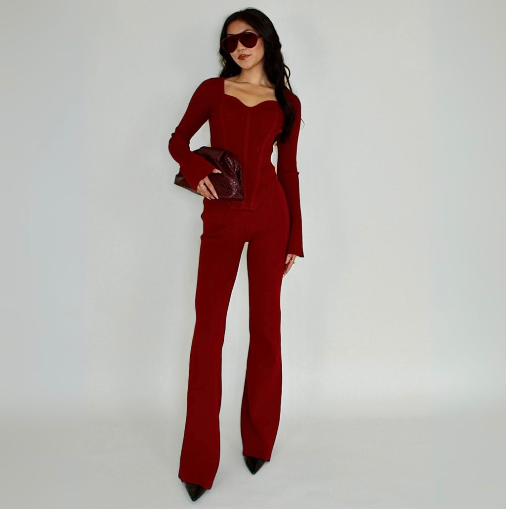 Woman wearing a red knit lounge top holding a clutch against a white background