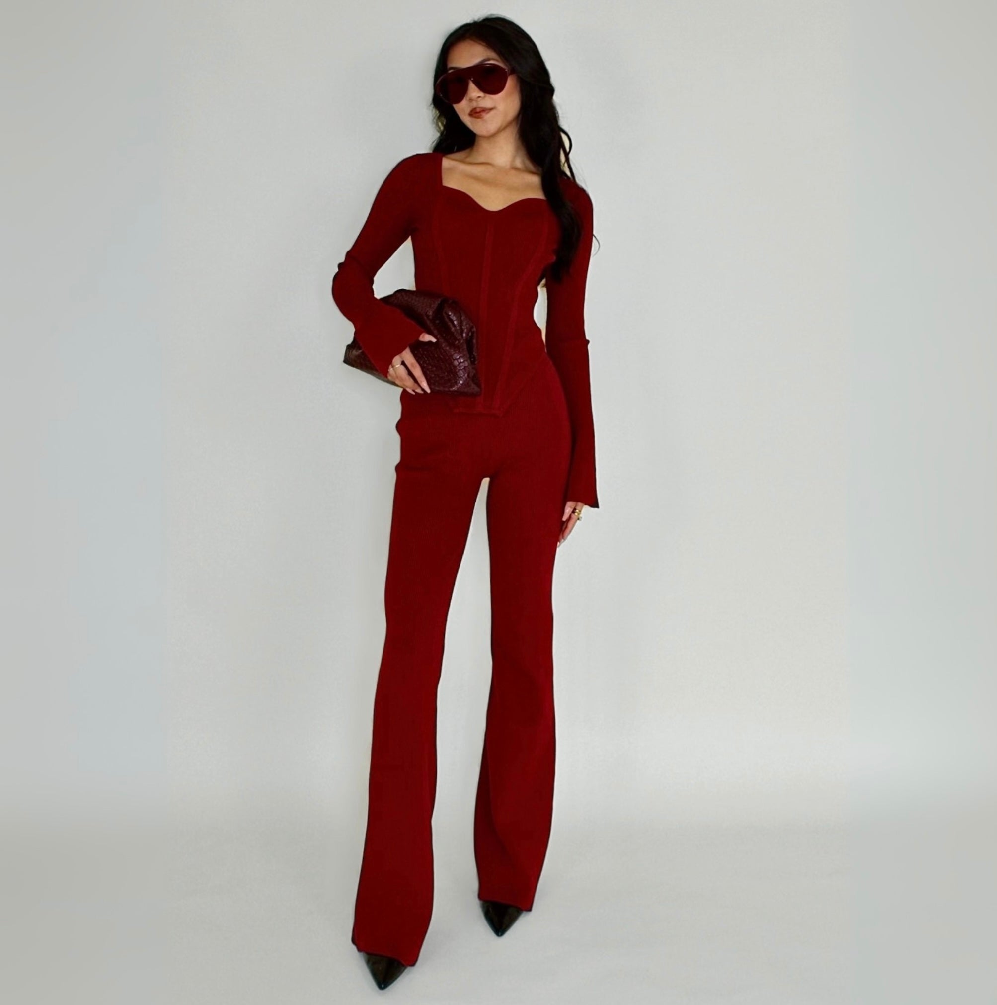 Woman wearing a red knit lounge top holding a clutch against a white background