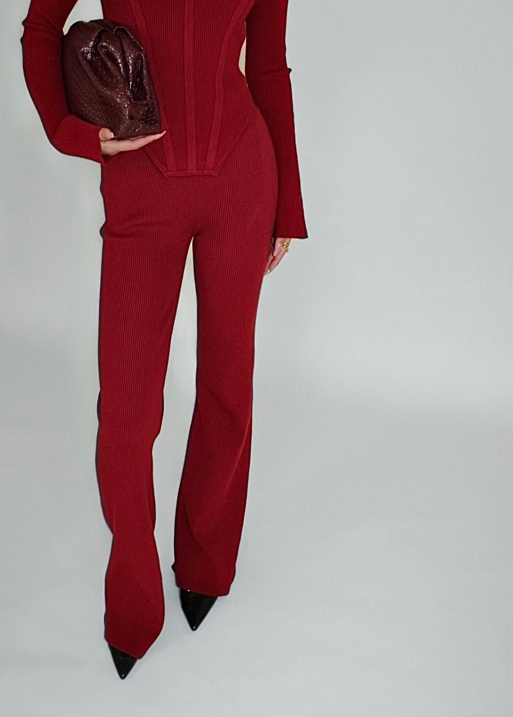 Person wearing a red lounge pant with a matching clutch on a plain background