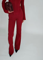 Person wearing a red lounge pant with a matching clutch on a plain background