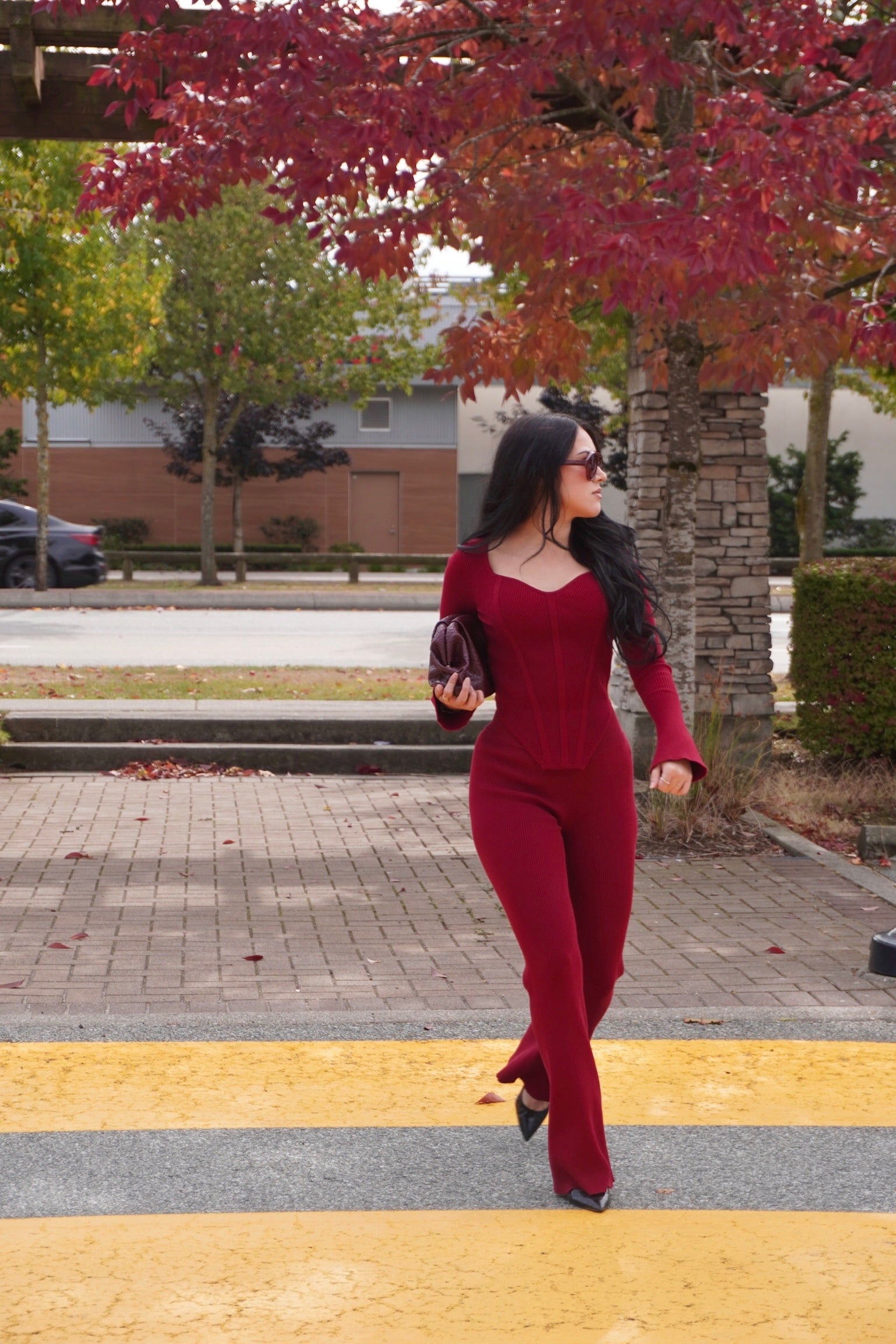 Woman in a red loungewear set crossing a street with autumn trees in the background