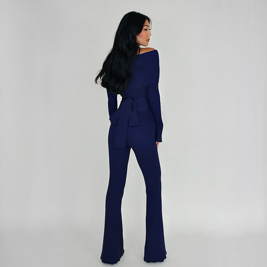 Woman wearing a navy blue jumpsuit against a plain background