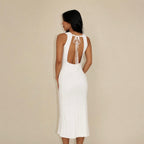 Woman wearing a white lounge dress with an open back against a beige background
