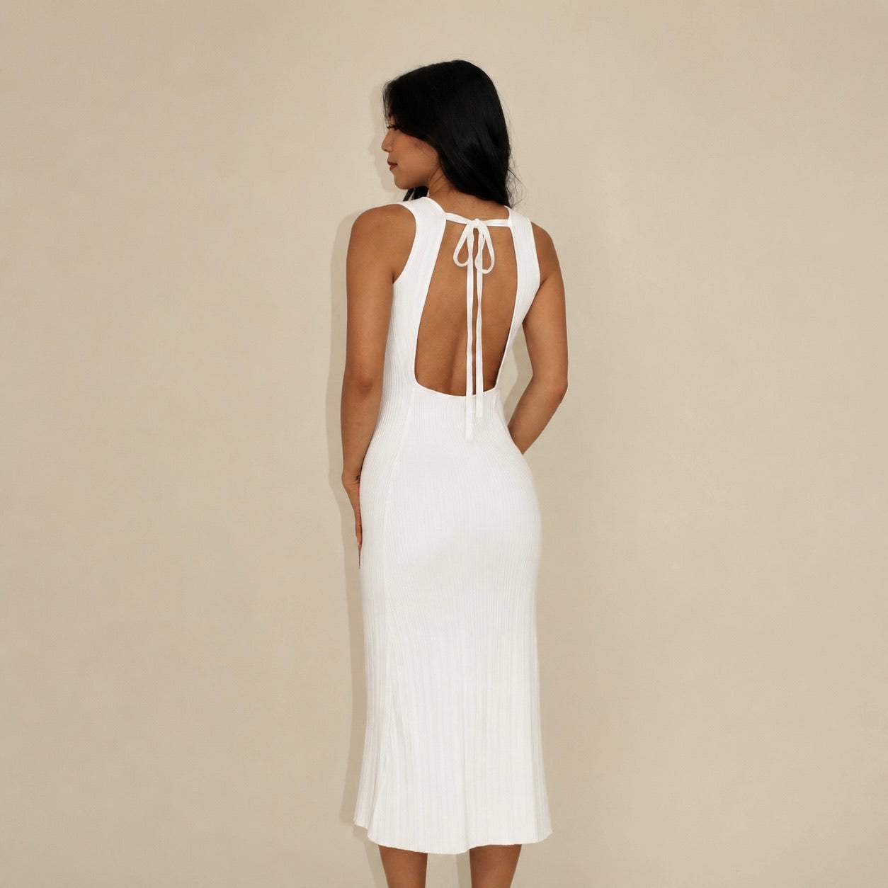 Woman wearing a white lounge dress with an open back against a beige background