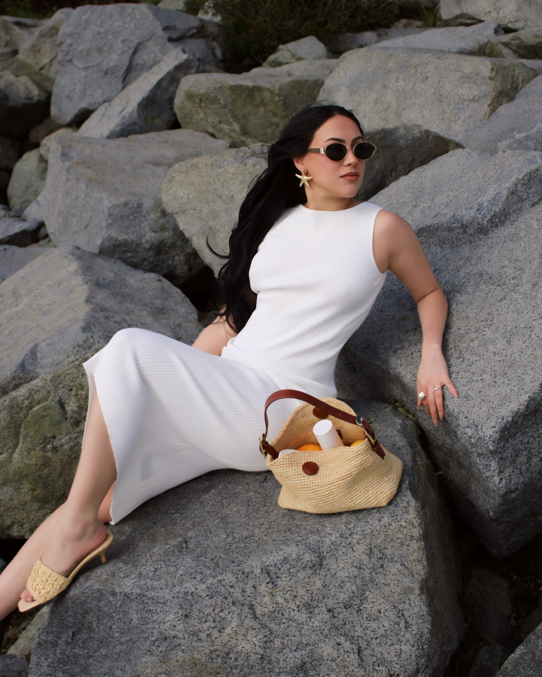 Woman in a white lounge dress sitting on rocks by the beach